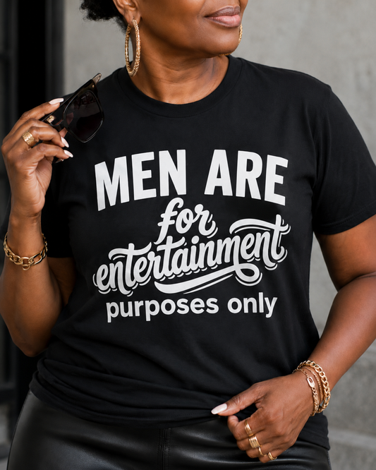 Person wearing a black t-shirt with white text that says men are for entertainment purposes only, holding sunglasses.